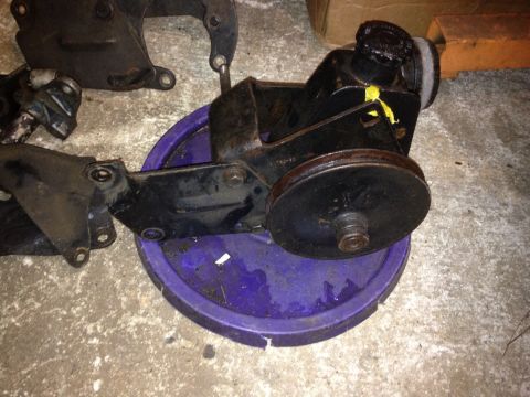 1994 Ford Bronco - A power steering pump assembly with a pulley sits on a purple bucket, with other parts in the background.