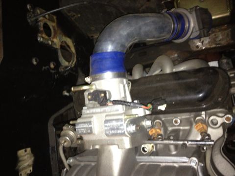 1994 Ford Bronco - A silver throttle body assembly is connected to an engine's intake manifold.