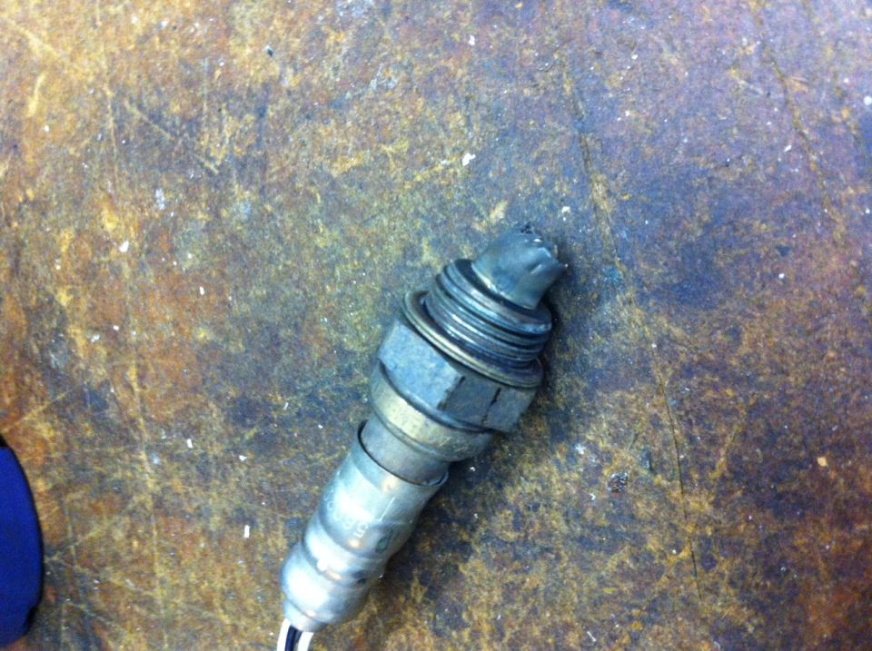 Exhaust oxygen sensor with damaged tip, resting on a textured surface