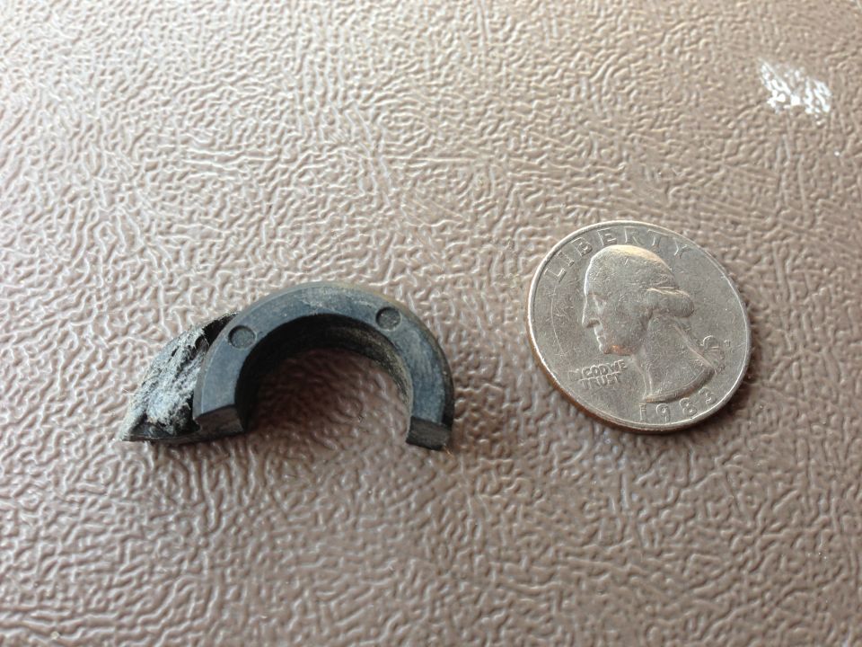 Damaged black rubber part next to a 1983 quarter