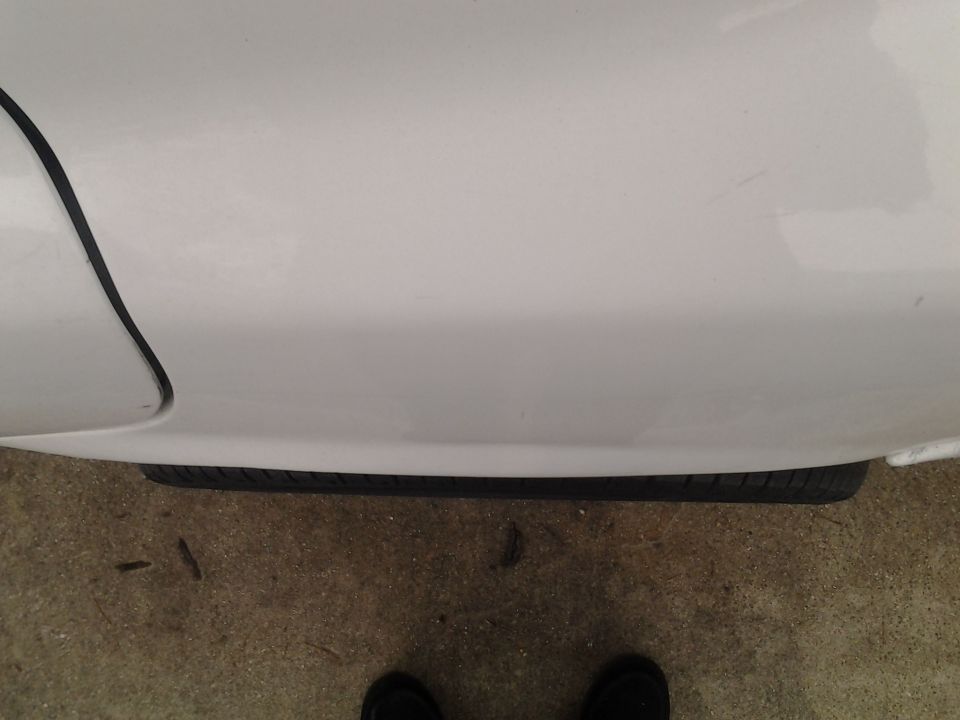 Close-up of a white car's fender and tire on concrete