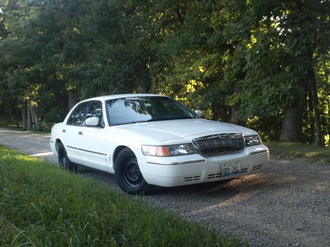 2000 Mercury Grand Marquis - A white 2000 Mercury Grand Marquis is parked on a gravel road surrounded by trees.