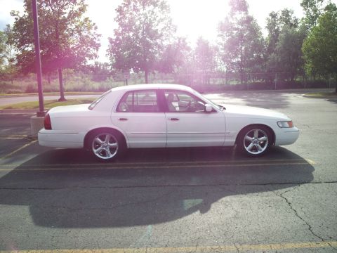 2000 Mercury Grand Marquis - A white sedan is parked in a lot on a sunny day, casting a shadow.