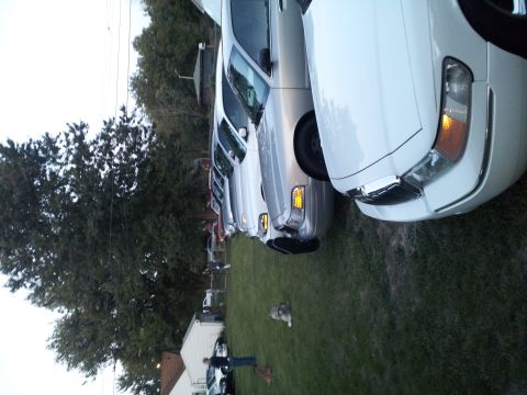 2000 Mercury Grand Marquis - Several cars are parked in a row on a grassy area, with a white Mercury Grand Marquis in the foreground.