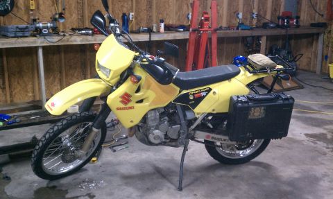 1989 Ford Bronco - A yellow Suzuki DR650 motorcycle is parked in a garage, equipped with saddlebags and a rear rack bag.