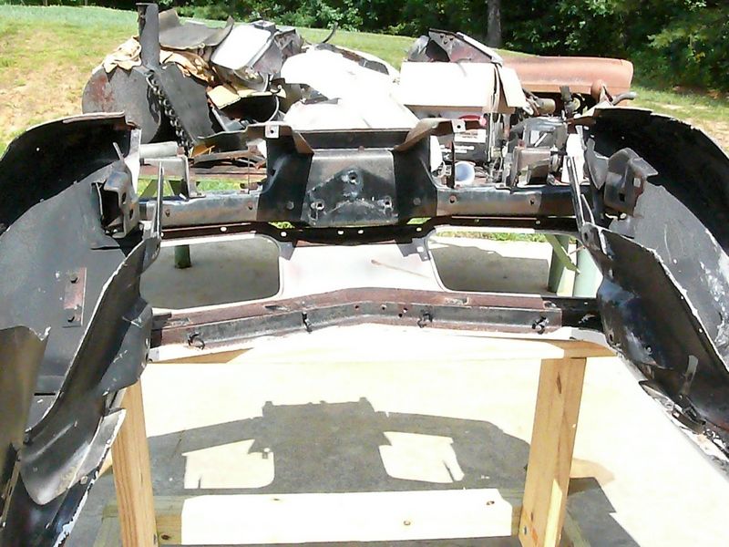 Car frame and bumper parts on sawhorses, with debris in background