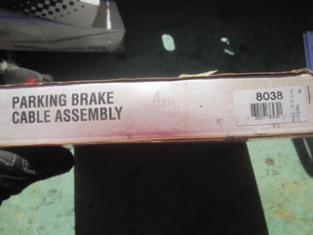 1993 Ford Bronco - A box containing a parking brake cable assembly is held in a gloved hand.