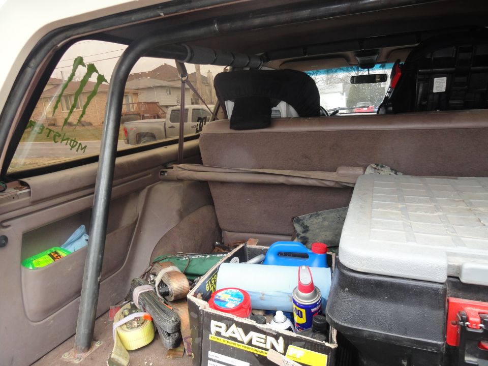 Interior view of a vehicle's cargo area with a roll cage, straps, and a toolbox. Monster Energy stickers are on the rear window
