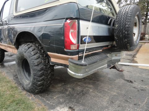 1995 Ford Bronco - Rear view of a dark green Ford Bronco with a spare tire and off-road modifications.