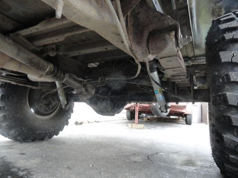 1995 Ford Bronco - Close-up view of the rear suspension and drivetrain components of a vehicle, showing the axle, leaf springs, and shock absorber.