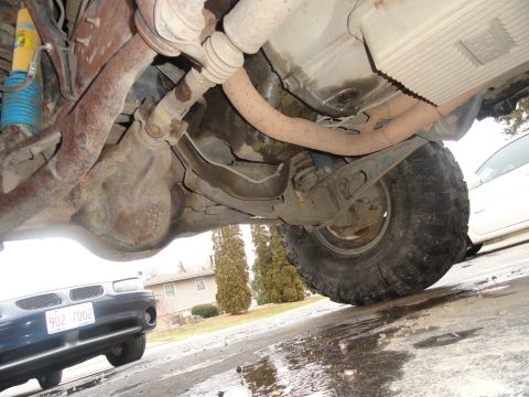 1995 Ford Bronco - The underside of a vehicle, including its drivetrain and suspension components, is visible along with a parked car.