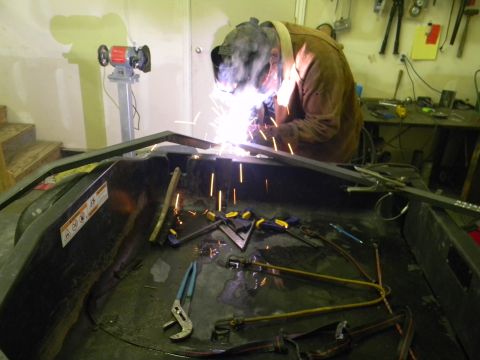 1990 Chevrolet Suburban - A person in protective gear welds a metal frame, with tools and a grinder visible in the background.