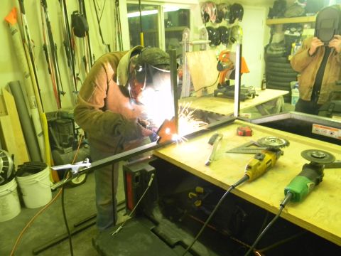1990 Chevrolet Suburban - A person is welding a metal frame in a workshop, with various tools and equipment visible in the background.