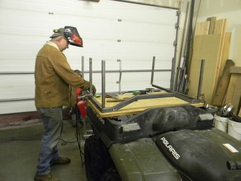 1990 Chevrolet Suburban - A person in welding gear works on a metal frame attached to the back of a green Polaris ATV.