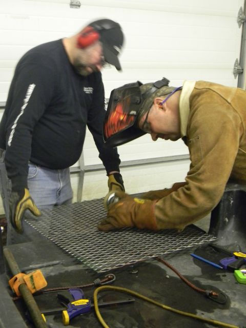 1990 Chevrolet Suburban - Two men are working on a metal grate, with one person welding and the other observing.