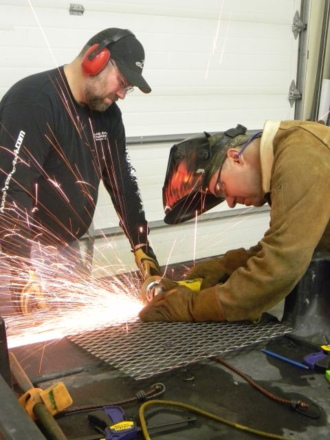 1990 Chevrolet Suburban - Two men are engaged in metalworking, one using an angle grinder while the other wears a welding mask, amidst a shower of sparks.