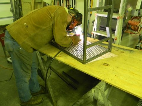 1990 Chevrolet Suburban - A person is welding a metal frame on a workbench in a workshop.