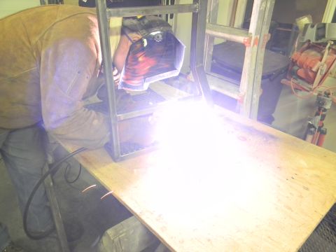 1990 Chevrolet Suburban - A welder is actively working on a metal structure, creating a bright display of sparks.
