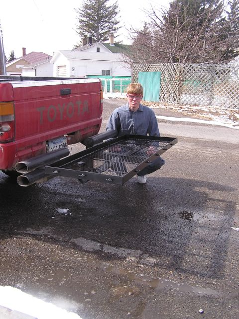 1994 Ford Bronco - A person kneels beside the rear of a red Toyota pickup truck, which is equipped with a cargo carrier and dual exhaust pipes.