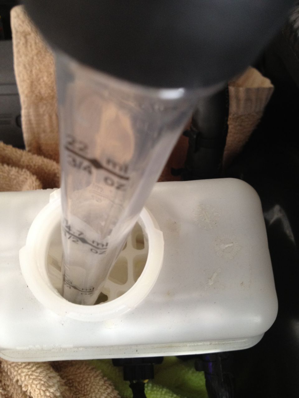 White plastic brake fluid reservoir with a clear measuring tube inserted, showing markings for ml and oz