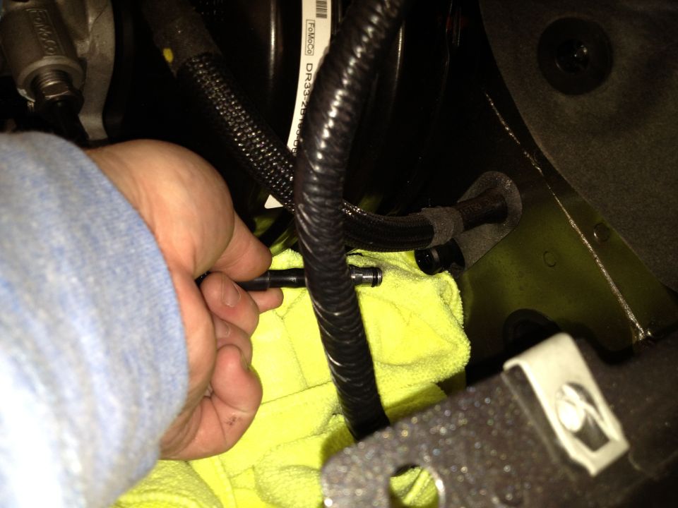 hand disconnecting a fuel line with a yellow cloth underneath