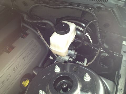 2013 Ford Mustang - Close-up of the brake fluid reservoir and master cylinder assembly in an engine bay.