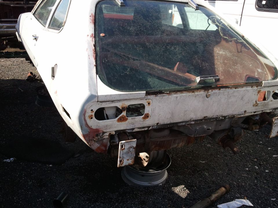 White car's rusty rear end with missing taillights, supported by a wheel rim