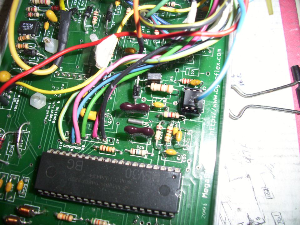 Close-up of a green circuit board with many colorful wires connected to various electronic components and a large black chip