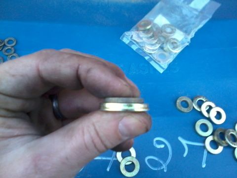 1981 Ford Bronco - A hand holds a washer with an insert; loose washers are visible on a blue surface.