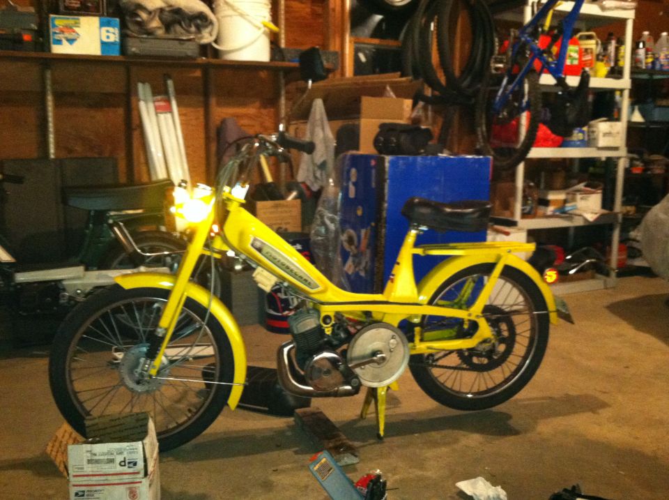 Yellow moped with black seat and handlebars, parked in a garage