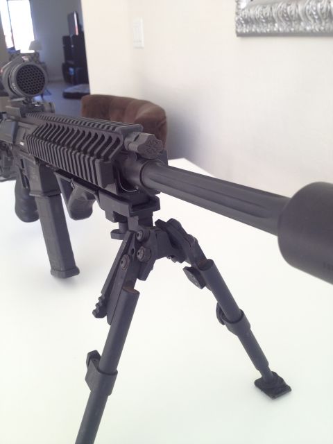 2013 Ford Mustang - Close-up of a tactical rifle with a bipod and scope, resting on a white surface.