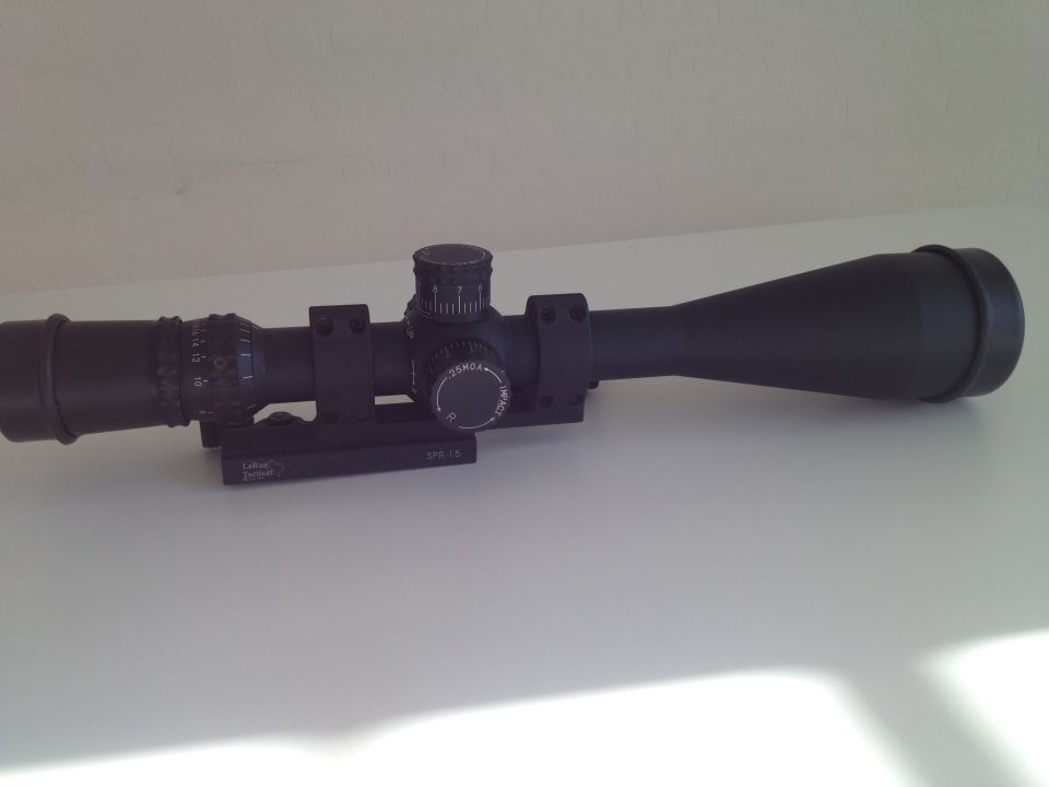 Rifle scope with turrets and markings on a white surface. Supermotors.net logo in corner