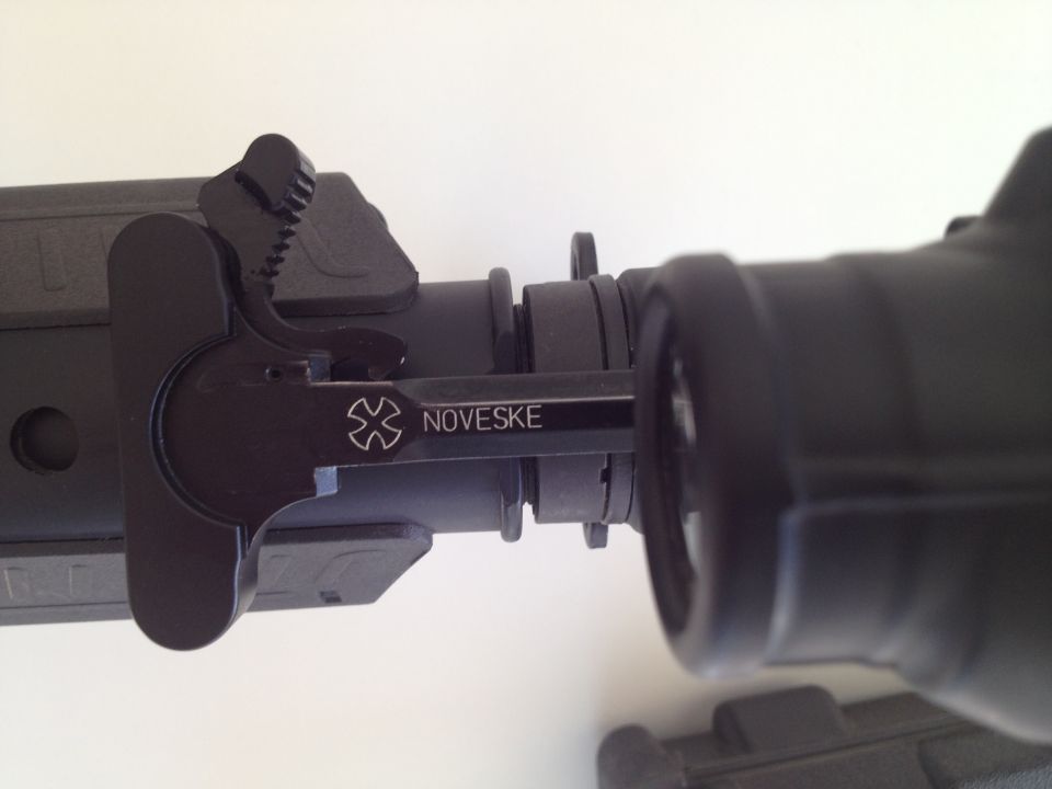 Close-up of a black AR-15 charging handle with the Noveske logo and name etched on it