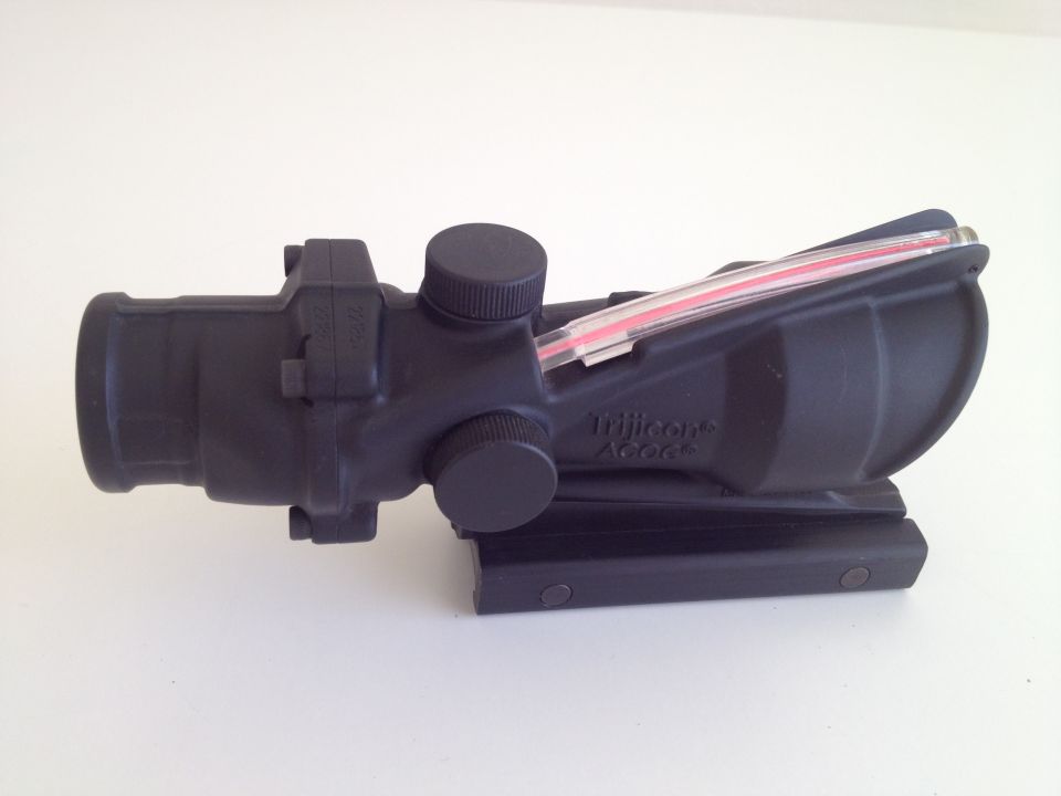 Black Trijicon ACOG scope with red aiming reticle, mounted on a black rail