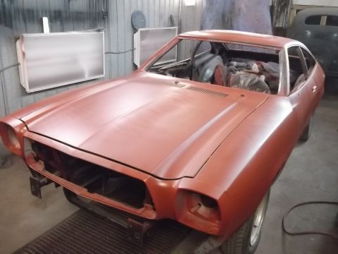 1978 Ford Mustang II - Orange coupe in a workshop, missing front-end components, appears to be undergoing restoration.