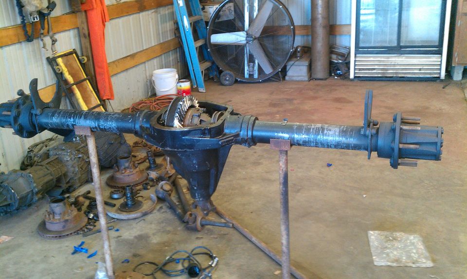 Differential axle assembly on stands, showing gears and axle shafts. Other parts and tools in background