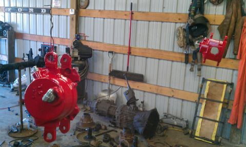1995 Ford Bronco - A red steering gear box is suspended in a workshop, with a 'Ford' sign visible on the wall.