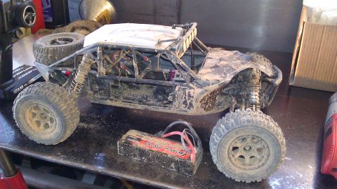 1996 Ford Bronco - A dirty remote control buggy sits on a workbench next to its battery pack and a spare tire.