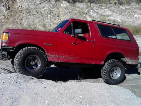 1988 Ford Bronco - Red Ford Bronco navigates a dirt and gravel terrain, showing its off-road capabilities.