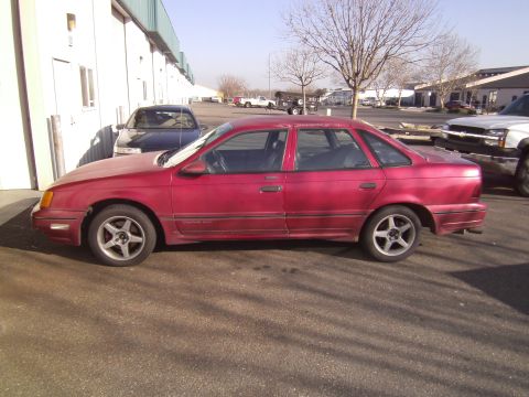 1991 Ford Taurus - A red 1991 Ford Taurus is parked outside a commercial building.