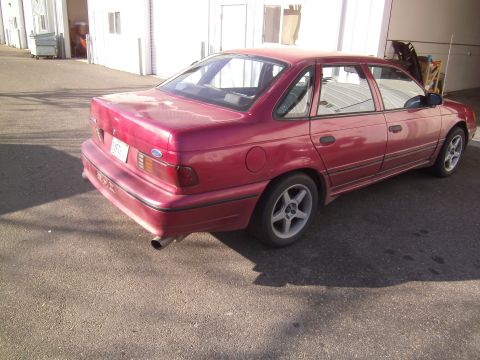 1991 Ford Taurus - A red sedan is parked outside a building, showing its rear and side profile.