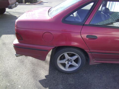 1991 Ford Taurus - Rear view of a red 1991 Ford Taurus sedan, showing the quarter panel, wheel, and part of the rear bumper.