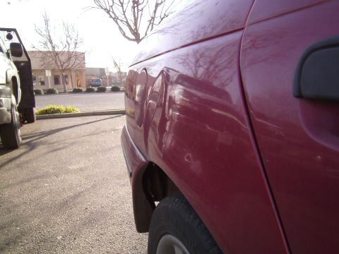 1991 Ford Taurus - Side view of a red car's damaged rear quarter panel, with another vehicle visible.