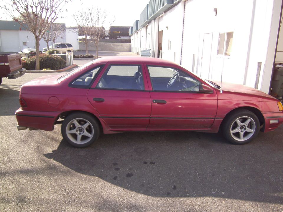 Red 1991 Ford Taurus sedan parked on asphalt, side view, showing minor wear