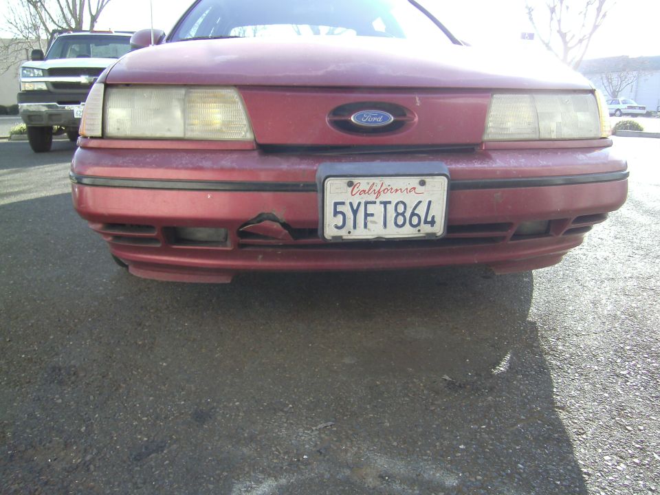Front view of a red 1991 Ford Taurus with a damaged bumper and a California license plate