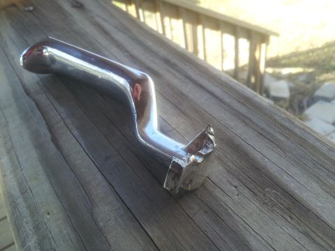 1986 Ford Bronco - Chrome door handle with a bent shaft and chipped mounting base, resting on wooden planks.