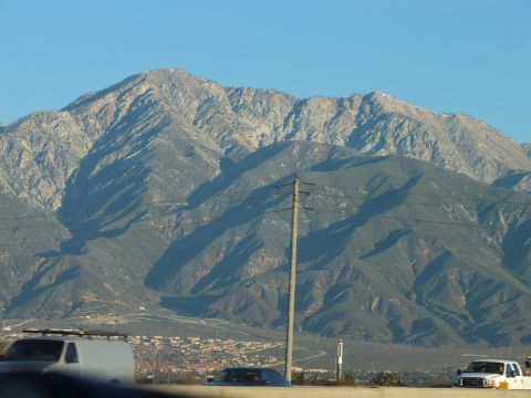 2003 Ford Crown Victoria - Steep tree-dotted mountain ridge behind a freeway, a power pole and white van and pickup in the foreground