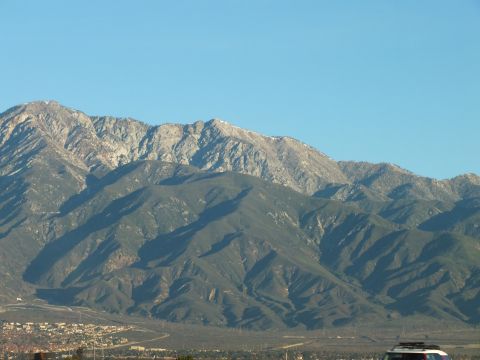 2003 Ford Crown Victoria - Sunlit mountain ridgeline with pale rocky summits above darker tree-covered slopes and distant houses