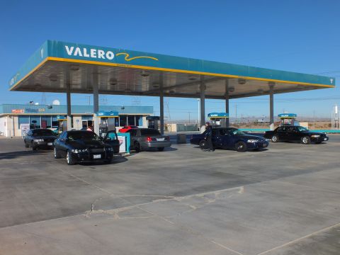 2003 Ford Crown Victoria - Wide view of a Valero fuel station with multiple black and silver sedans gathered on the concrete lot