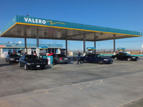 2003 Ford Crown Victoria - Valero station with a row of black sedans at the pumps and a person crossing the concrete apron
